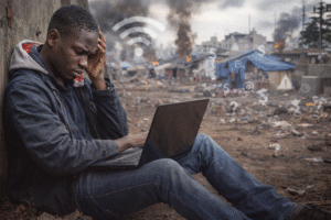 Jeune habitant de Goma utilisant son ordinateur portable dans un environnement précaire, symbole des « réfugiés numériques » qui cherchent des opportunités en ligne malgré les conséquences de la guerre à l’est de la RDC.